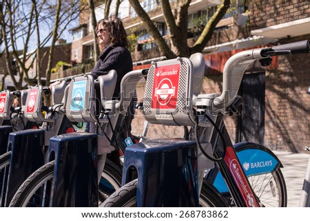 London, UK - April 12 2015: Detail of Boris bikes in line with woman in the background.  In 2015, Mayor Boris Johnson announced Santander as new Cycle Hire sponsor which will replace Barclays bank.