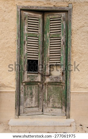 Old wooden door with a square hole and a rusty chain as a locker. The green painting of the door is coming off leaving the grey old wood on view.