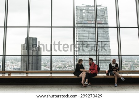 London, UK - June 28 2015: Couple holding hands and man looking at ipad on the rooftop garden of the Walkie Talkie. In background glass window facing the Tower 42 and the Leadenham skyscrapers.