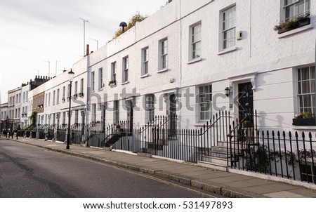 View of an empty street in the residential area of Chelsea, London, UK with Victorian white residential buildings with black doors and metal fence.