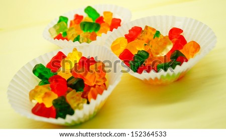 Colorful gummy bears in white paper party cups on yellow background for birthday card design or party invitation.