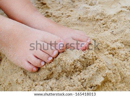 Small Child\'s Feet in the Sand.  A small child\'s feet rest in the sand at the beach.
