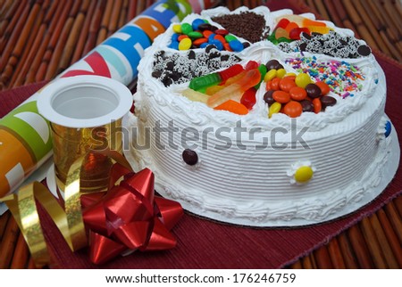 Birthday Cake, Ribbons and Bows.  A traditional birthday cake decorated with assorted candy next to party decorations wrapping paper, ribbon and a bow.