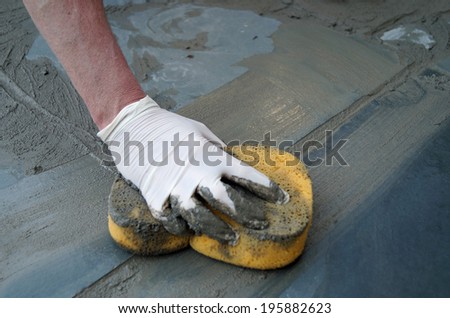 Man Fixing Sidewalk.   A man uses a sponge to spread wet cement on a cracked sidewalk.