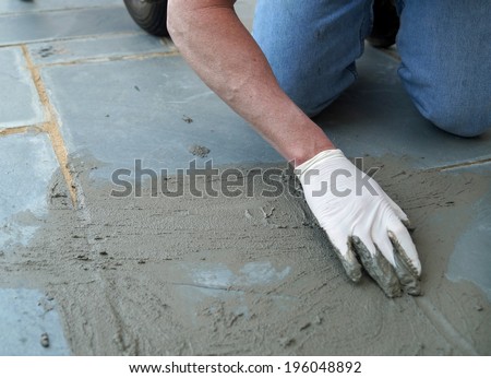 Home Improvement Project.  A man working on a home improvement project spreads wet cement on a cracked sidewalk.