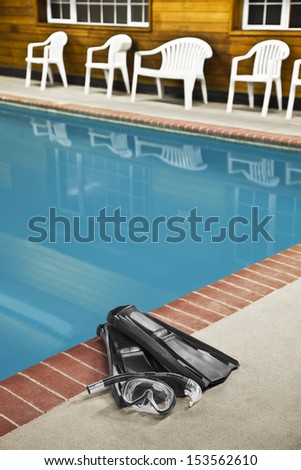 Swimming aides include goggles, snorkel, and fins sitting on the edge of the pool waiting to be used. The shorter depth of field focuses on the swim gear in the foreground.