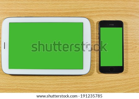Smart phone and white digital tablet computer on wooden desk.