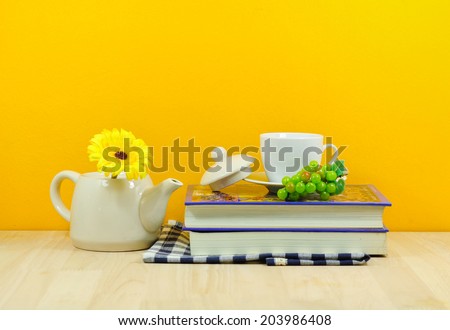 home decor: a stack of books, flowers and teapot on a yellow wall shelf
