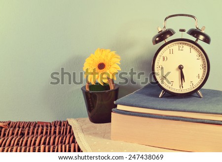 Old alarm clock with  books and yellow flower  vase on wood basket texture