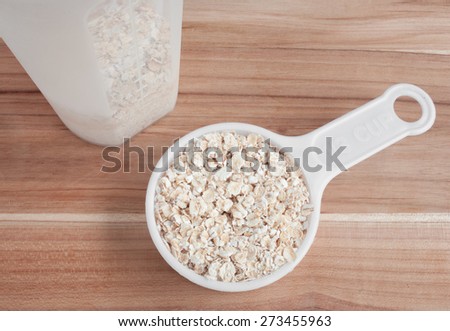 Measuring scoop and cup of oats on wooden table surface.