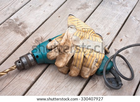 Power drill and work gloves on wooden boards