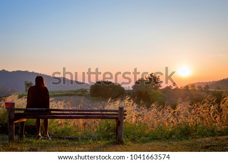 Romantic woman sitting on the wooden chair.Asian girl looking at sunrise in the morning on mountain ,Suphanburi province,Thailand.Lonely girl with nature concept.