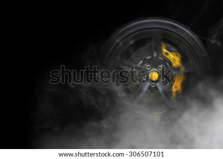 Isolated generic sport car wheel with yellow breaks drifting and smoking on a black background