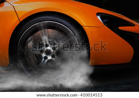 Orange super sport car from side with detail on spinning wheel, smoking and doing burnouts on a dark background