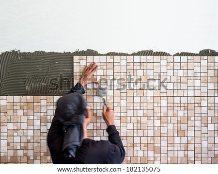 Man installing ceramic wall tile with a rubber hammer