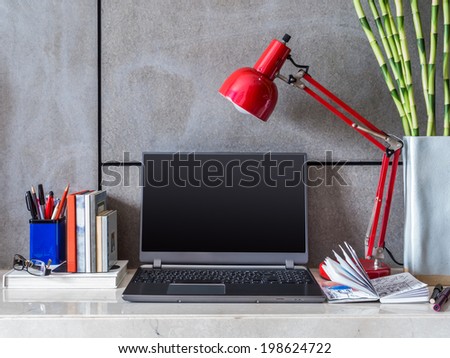 Modern home office desk with laptop, lamp and vase of flowers