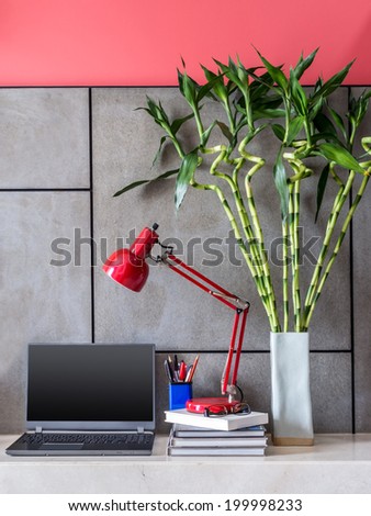 Modern office desk with laptop, lamp and vase of  Lucky bamboo