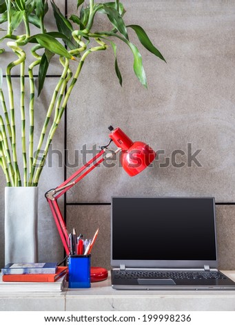 Laptop, lamp with vase of Lucky bamboo on desk in modern room