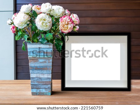 Flowers vase and blank black picture frame on wooden desktop