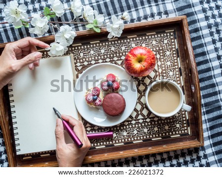 Hands writing on notebook with tea cup, appetizer in wooden tray