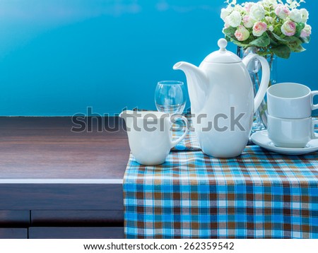 Artificial flower vase, teapot and dishware on wooden cupboard/ interior still-life