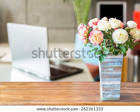 Artificial flower vase on table top over blurred image of  modern workplace background