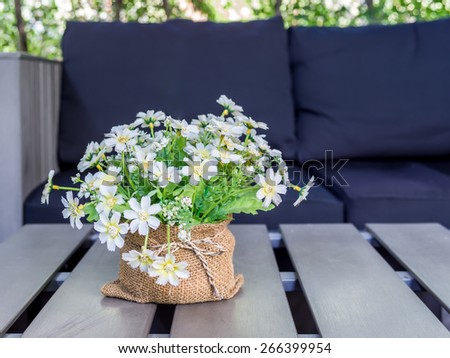 Artificial flower on desk top with black couch background