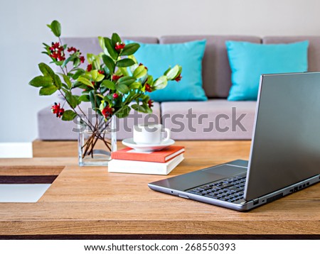 Laptop, flower vase on table top with sofa background/ modern interior Living room