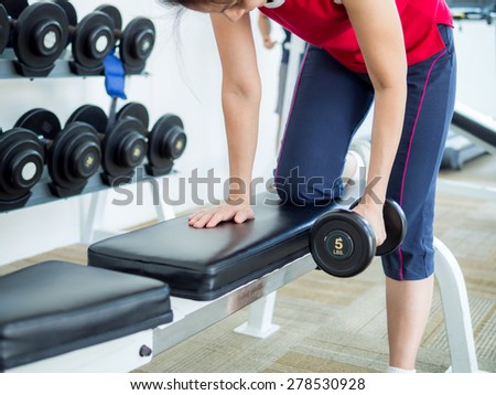 Young woman exercising with lifting dumbbell in gym