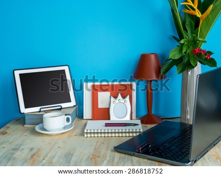 Still life of modern colorful interior workspace with laptop, tablet, flower vase