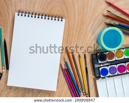 Top view of blank  sketchbook, watercolor paints, color-pencils for painting on  wooden background