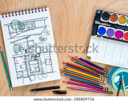 Top view of watercolor paints, color-pencils for painting with architectural  sketchbook on  wooden background