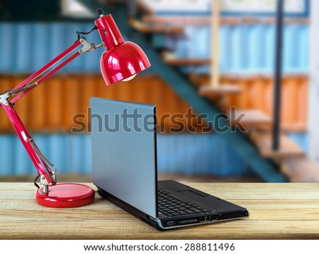 Red lamp, laptop on wooden counter top with artistic modern staircase blurry background