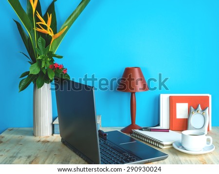 Still life of modern colorful interior workspace with laptop, flower vase, coffee cup