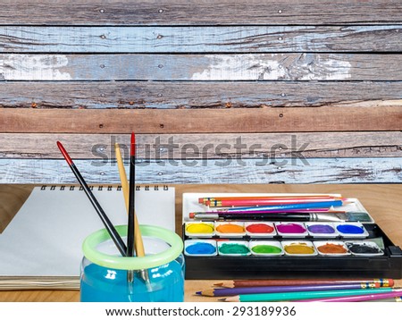 Watercolor box and equipment for artist  painting on wooden tabletop over rustic wood wall  background