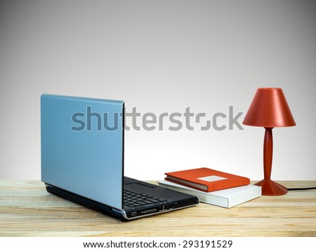Red lamp with laptop computer, books on wooden table top over grey wall background/ interior still life
