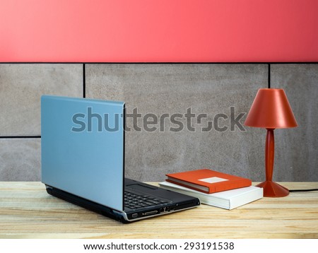 Red lamp with laptop computer, books on wooden table top over modern wall background/ interior still life
