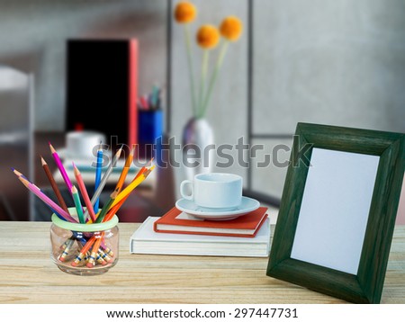 Photo frame, books, coffee cup, color pencils on wooden table over defocused office background/ interior still life