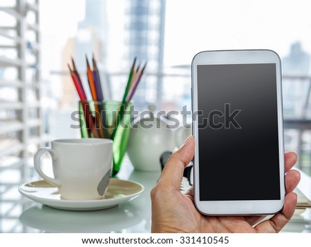 Hand holding cell phone with working table background in office scene
