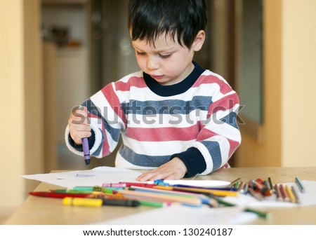 Portrait of a small child, boy or girl, drawing and playing with colorful crayons, pens and pencils.