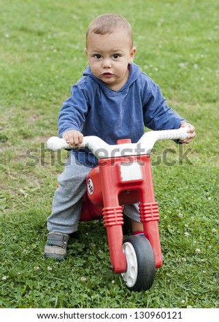 A small boy playing outside with a plastic toy motorbike.