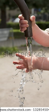 Hands of child playing with water in street water fountain.