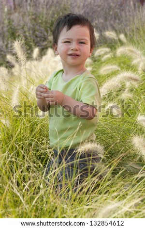 A small child standing in a long grass in a Mediterranean garden.
