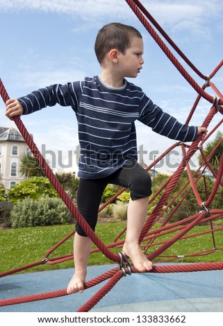 Child playing barefoot at playground on a rope climbing frame equipment.