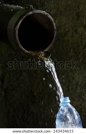 Old rustic water pipe with running drinking water and plastic bottle being filled up, aid concept.