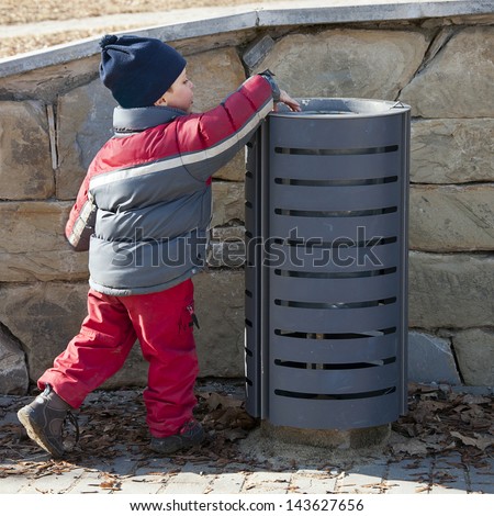 Small child putting a waste or litter in a street rubbish can or bin.