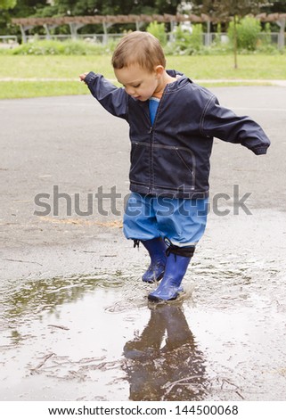 Happy child toddler playing in puddle after the rain.