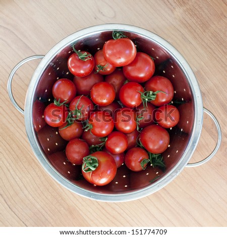Tomatoes, freshly picked and washed in colander on wooden table, top view.