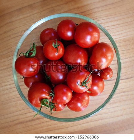 Tomatoes, freshly picked and washed in glass bowl on wooden table, top view.