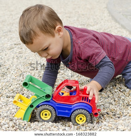 Toddler child boy playing with a plastic toy digger car.